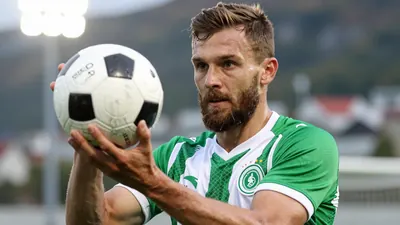 A 30-year-old, bearded, Molde football player in a green and white jersey, with a determined expression, holding a...